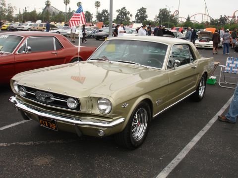 1993 Ford Taurus - A gold 1965 Ford Mustang is parked at a car show with other vehicles and people.