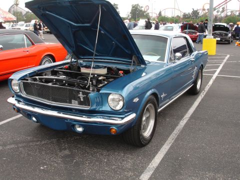 1993 Ford Taurus - A blue 1965 Ford Mustang coupe is parked with its hood open, revealing the engine bay.