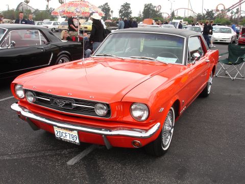 1993 Ford Taurus - A bright orange 1965 Ford Mustang coupe with a black roof is parked at an outdoor event, with other vehicles and people in the background.