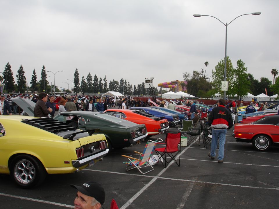 Yellow and green classic cars parked in a lot, people milling around