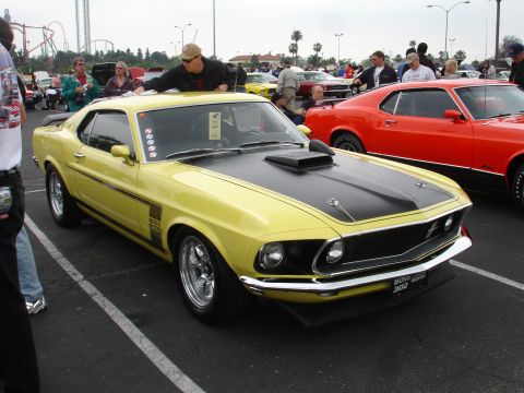 1993 Ford Taurus - A yellow 1969 Ford Mustang Boss 302 is parked next to a red car at an outdoor event.