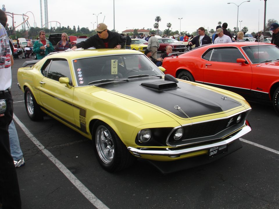 Yellow 1969 Ford Mustang Boss 302 with black hood stripes and scoop, chrome wheels, and a black front spoiler