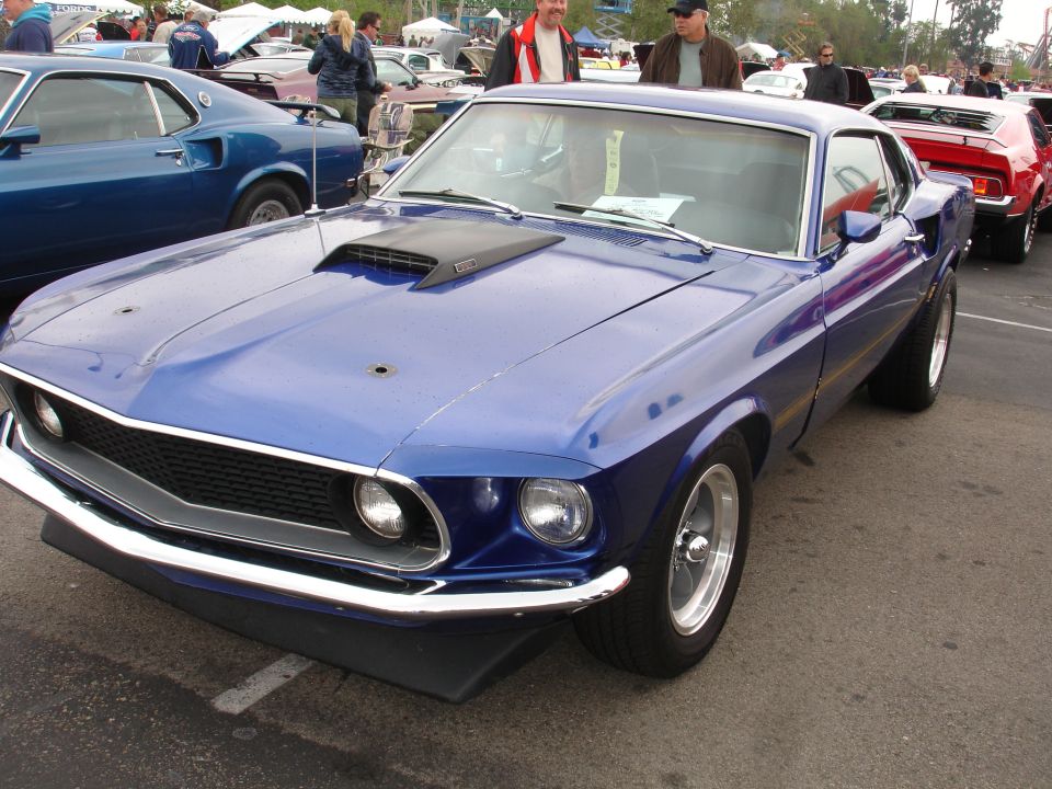 Blue 1969 Ford Mustang with a hood scoop and chrome bumper parked at a car show