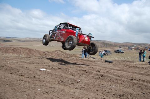 1992 Ford Explorer - A red off-road buggy soars through the air during a race event with spectators gathered.