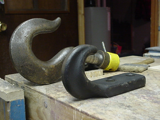 Two metal tow hooks, one large and rusty, the other black with a yellow cap on a bolt