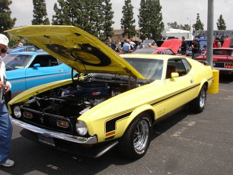 1993 Ford Taurus - A yellow 1971 Ford Mustang Mach 1 is displayed with its hood up, revealing the engine. Other vehicles are visible in the background.