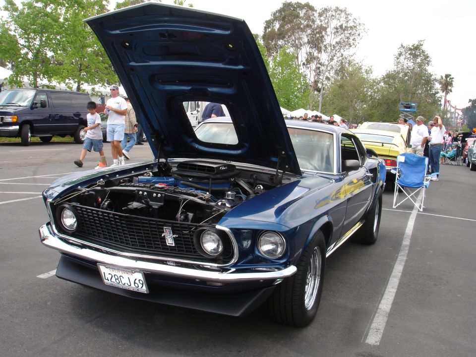 Blue 1969 Ford Mustang coupe with hood open, showing engine. Chrome bumper, black grille, and license plate L28CJ69 visible
