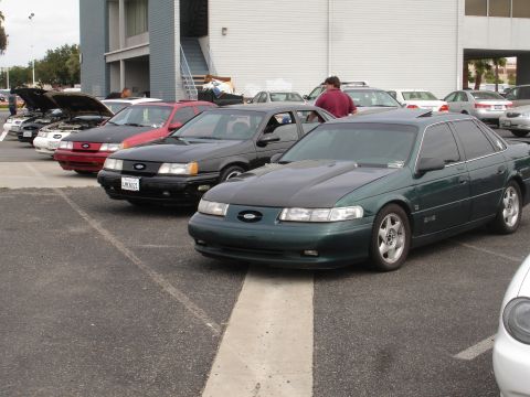 1993 Ford Taurus - A line of sedans, including a green 1993 Ford Taurus with a black hood, are parked in a lot.