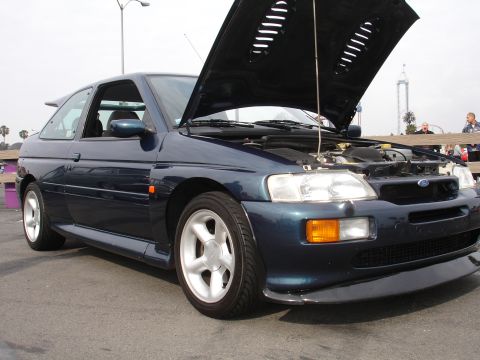 1993 Ford Taurus - A dark blue Ford Escort RS Cosworth is parked with its hood open, revealing the engine. The car has a sporty spoiler and distinctive wheels.