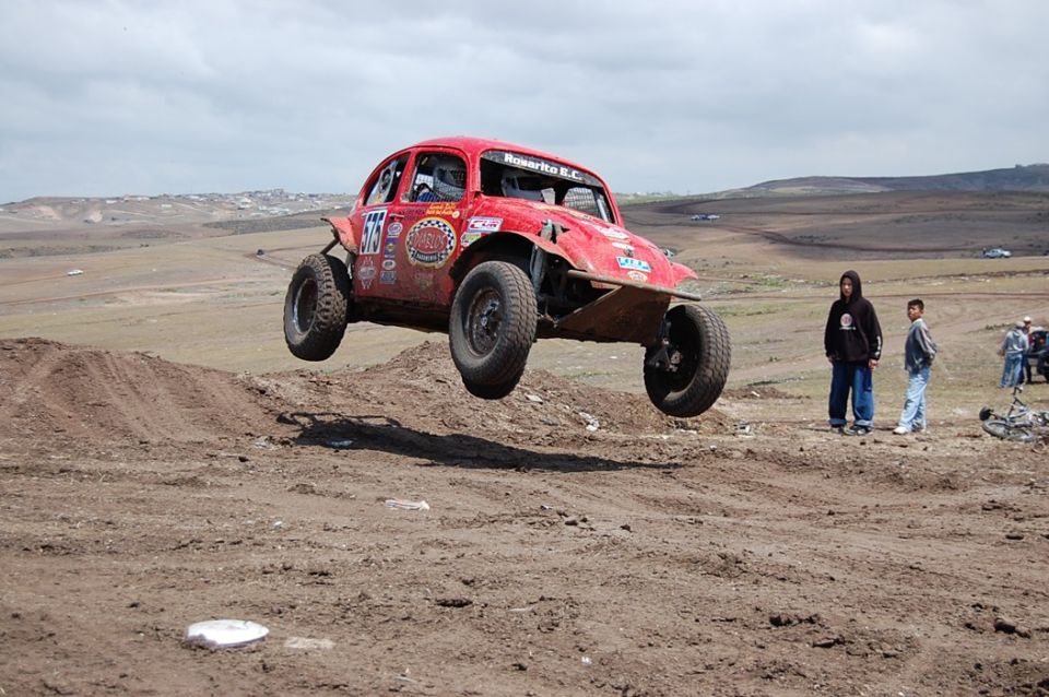 Red off-road buggy mid-air over dirt jump, number 575 on door, various stickers on body