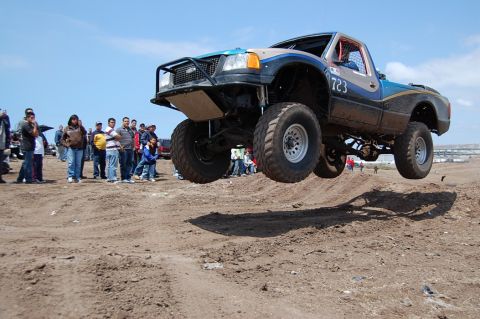 1992 Ford Explorer - A modified truck soars through the air during an off-road event, with spectators watching from the sidelines.