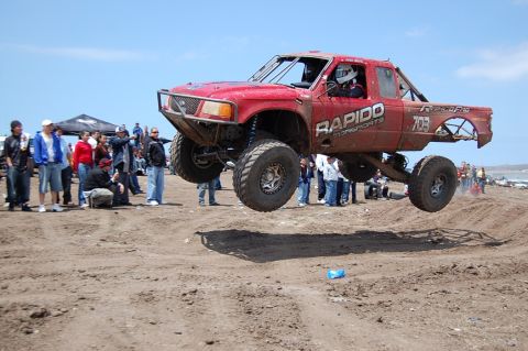 1992 Ford Explorer - A modified red truck soars through the air during a race event with spectators watching.