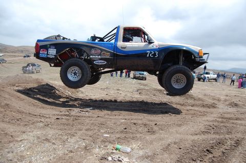 1992 Ford Explorer - A modified truck with large tires jumps over a dirt mound during a race event.