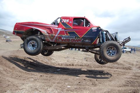1992 Ford Explorer - A red off-road racing truck with 'Almaraz Race Craft' livery is captured mid-air during a race.