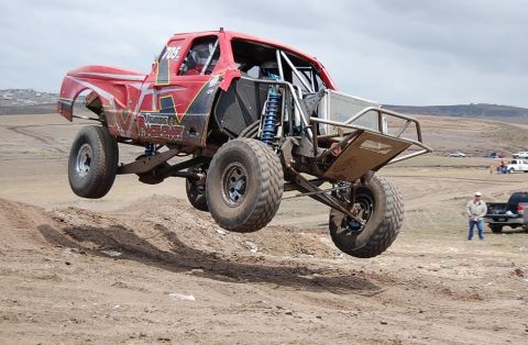 1992 Ford Explorer - A custom red off-road truck soars through the air over a dirt track during a race.