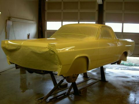 1967 Ford Ranchero - A car is covered in yellow masking paper, likely for painting, and is elevated on stands in a garage.