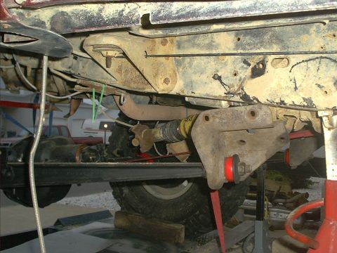 1986 Ford Bronco - Close-up of the undercarriage of a red vehicle, focusing on suspension components and a driveshaft.