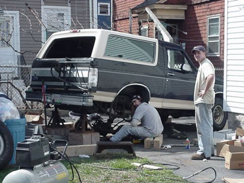 1993 Ford Bronco - Two men work on a 1993 Ford Bronco that is raised on jack stands in a driveway.