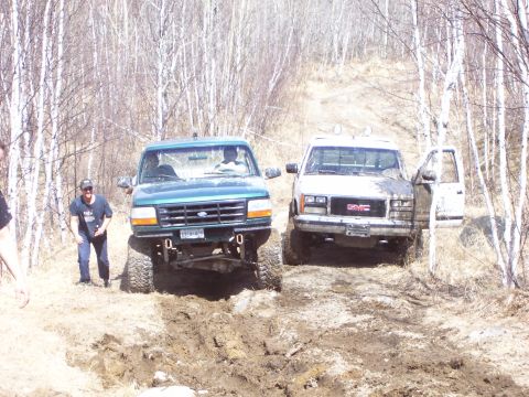 1996 Ford Bronco - A green 1996 Ford Bronco and a GMC truck navigate a challenging muddy off-road trail.