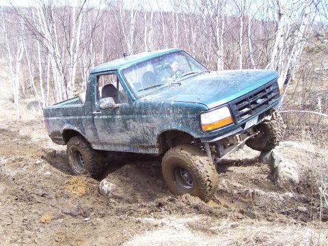 1996 Ford Bronco - Green 1996 Ford Bronco navigating a muddy off-road course with one wheel elevated.