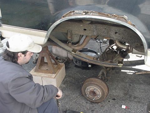 1993 Ford Bronco - A person works on the rear suspension of a vehicle that is supported by jack stands, with the wheel removed.