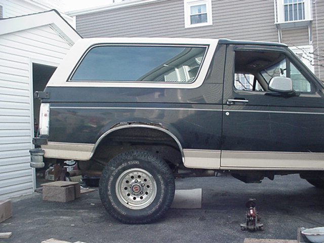 Dark green Ford Bronco on jack stands in a driveway with front wheel removed, side view