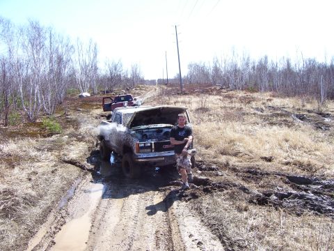1996 Ford Bronco - A GMC truck is stuck in the mud with its hood open, while another truck is visible in the background.