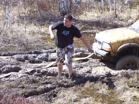 1996 Ford Bronco - A person attempts to pull a yellow SUV out of deep mud using a tow strap.