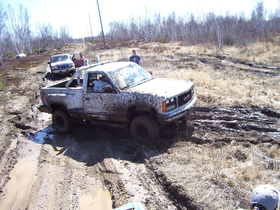 Muddy GMC pickup truck stuck in a muddy trail with other vehicles behind it