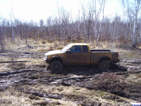 1996 Ford Bronco - Pickup truck is stuck in the mud, being pulled by a rope.
