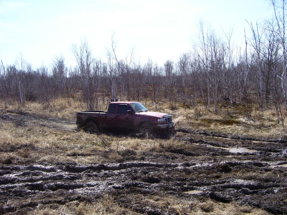 Red pickup truck stuck in mud, front 3/4 view. Grille suggests early 2000s model