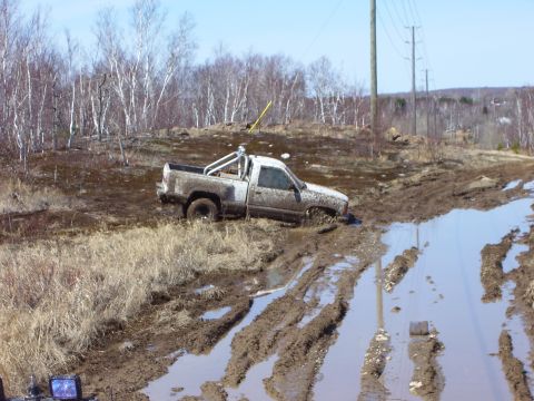 1996 Ford Bronco - A pickup truck is stuck in a muddy trail with water and ruts.