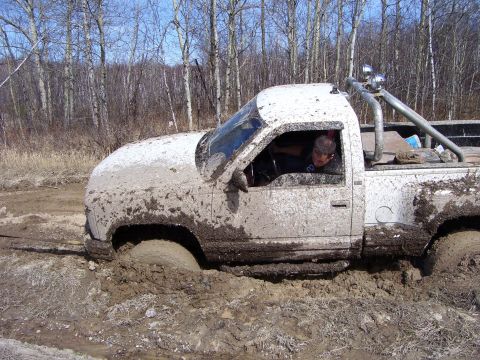 1996 Ford Bronco - A white pickup truck is deeply stuck in mud, with a person visible in the driver's seat.