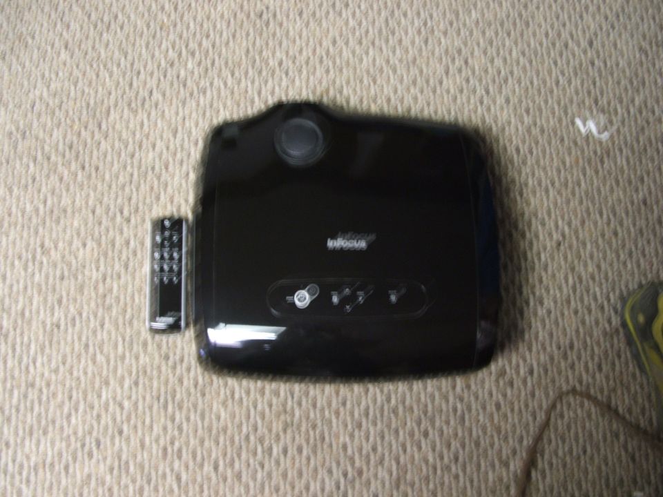 Black InFocus projector and remote control on a carpeted surface