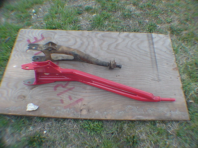 Rusty and red-painted suspension control arms on plywood in grass