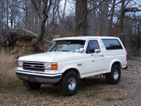 1989 Ford Bronco - White 1989 Ford Bronco parked on a gravel surface with trees behind it.