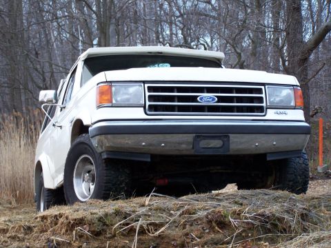 1989 Ford Bronco - This Ford Bronco is positioned on a rough terrain, with a backdrop of bare trees.