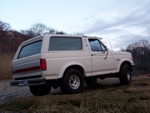 1989 Ford Bronco - This 1989 Ford Bronco is seen from the rear quarter angle, parked on uneven terrain under a cloudy sky.