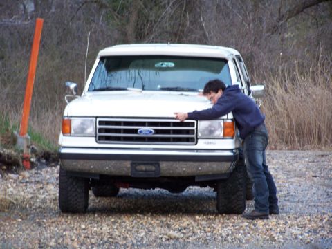 1989 Ford Bronco - Man embraces the front of a white Ford F-Series truck, likely from the late 1980s.