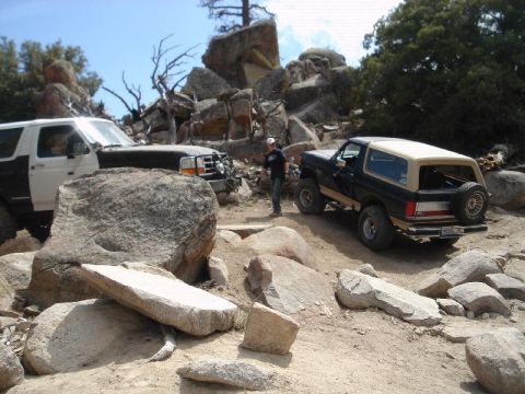 1994 Ford Bronco - A trail staging area among granite boulders and pines where a black lifted full-size Bronco with a tan hardtop, tan two-tone stripe and rea…