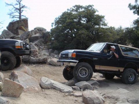 1994 Ford Bronco - Side view of a lifted dark blue Eddie Bauer-style Ford Bronco with tan lower two-tone and tan roof flexing over granite rocks on a pine for…