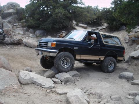 1994 Ford Bronco - Dark blue two-door Ford Bronco with a tan lower two-tone stripe and tan hardtop crawling over granite boulders on a rocky mountain trail, d…
