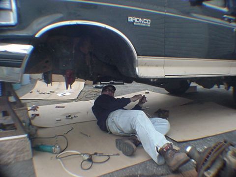 1993 Ford Bronco - Man works on the underside of a 1993 Ford Bronco, which is supported by jack stands.