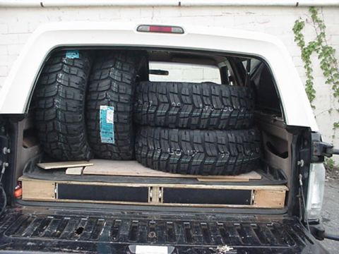 1993 Ford Bronco - Rear view through the open tailgate and raised glass of a full-size SUV with a white removable roof, loaded with four brand-new aggressive…