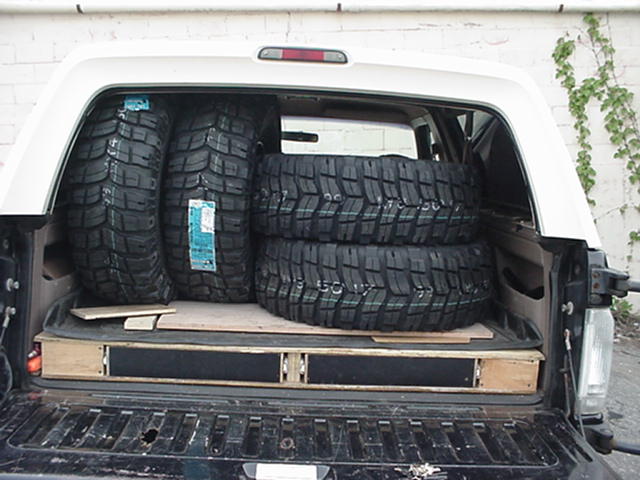 Four new mud-terrain tires loaded in the rear cargo area of an SUV with white top