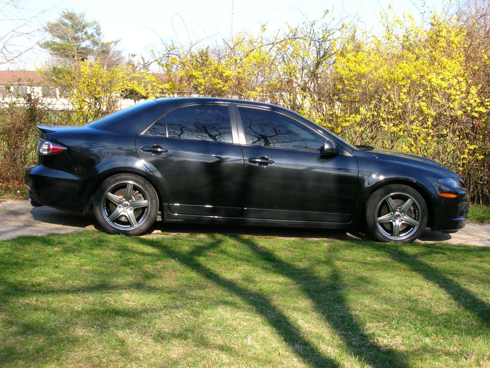 Black sedan parked on grass, side view. Tinted windows, aftermarket wheels, spoiler