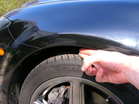 1994 Ford Probe - A hand is shown checking the clearance between the tire and the fender of a black vehicle.