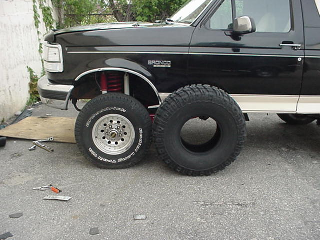 Black Ford Bronco jacked up beside stock wheel and taller mud tire