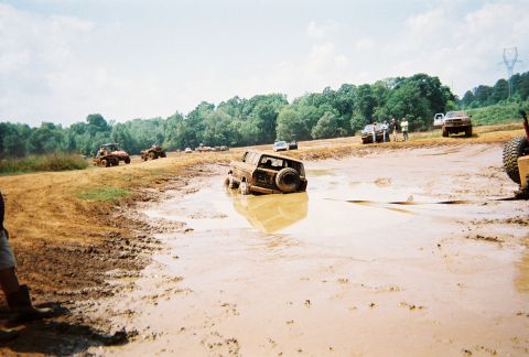 1978 Ford Bronco - Multiple vehicles navigate a muddy terrain, with one SUV deeply submerged in the mire.