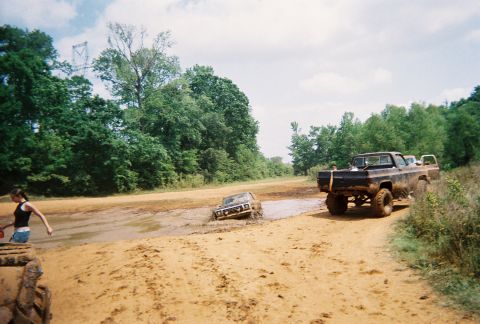 1978 Ford Bronco - Two trucks are stuck in a muddy track, with a woman standing nearby.